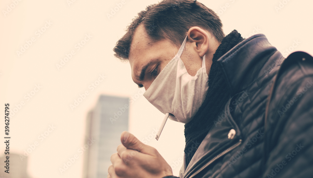 serious man in a protective mask smokes standing on the street. serious man in a protective mask smokes standing on the street.