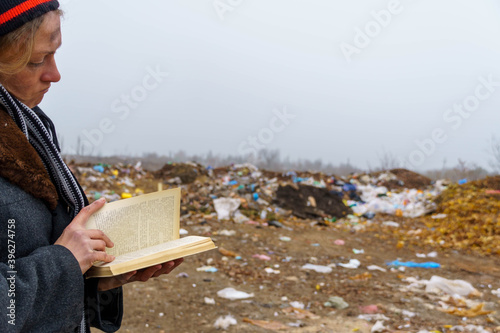 Homeless woman reads a book on the background of a junkyard.