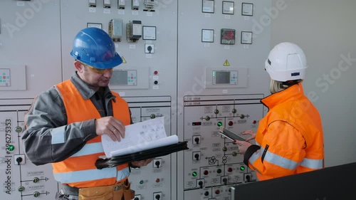 Engineer with papers shows female inspector with tablet installed new equipment at contemporary wind power plant substation