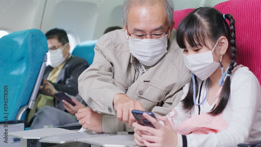 Obraz premium Asian grandfather is teaching to wear correctly the facial mask to his granddaughter.Coronavirus prevention on the airplane.travel concept