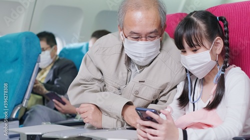 Asian grandfather is teaching to wear correctly the facial mask to his granddaughter.Coronavirus prevention on the airplane.travel concept