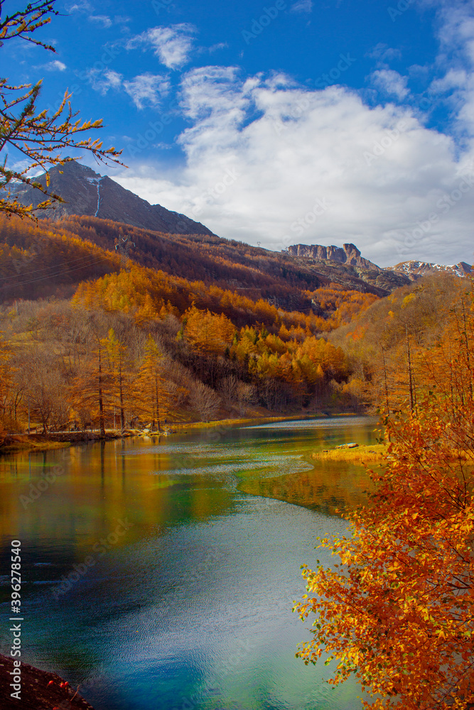 View of a mountain lake during autumn. Lake at the foot of the snow-capped mountains with flora tinged with autumn colors. View of a mountain lake during autumn. Lake at the foot of the snow-capped mountains with flora tinged with autumn colors.
