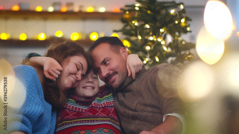 Happy mom, dad and preteen son embracing relaxing on couch in apartment decorated for christmas Happy mom, dad and preteen son embracing relaxing on couch in apartment decorated for christmas