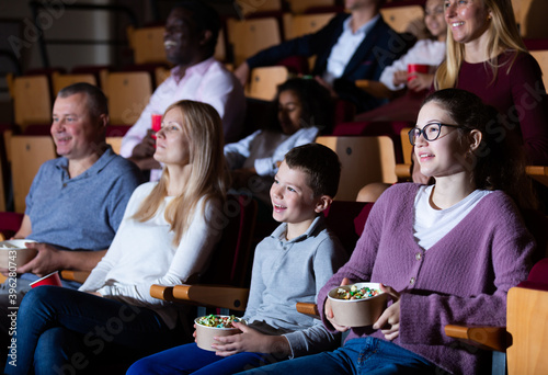 Portrait of friendly family eating popcorn and laughing while watching funny movie in cinema