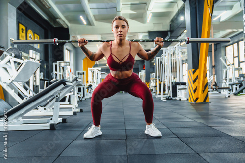 Focused sportswoman doing exercise with barbell while working out
