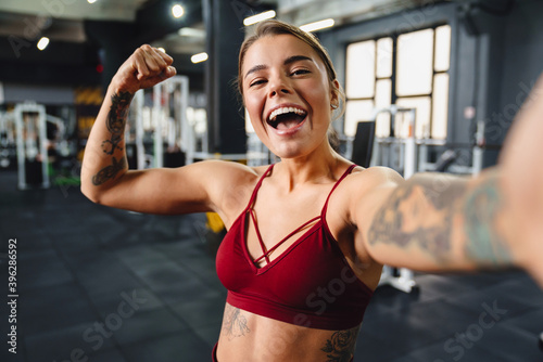Excited sportswoman showing her bicep and laughing while taking selfie
