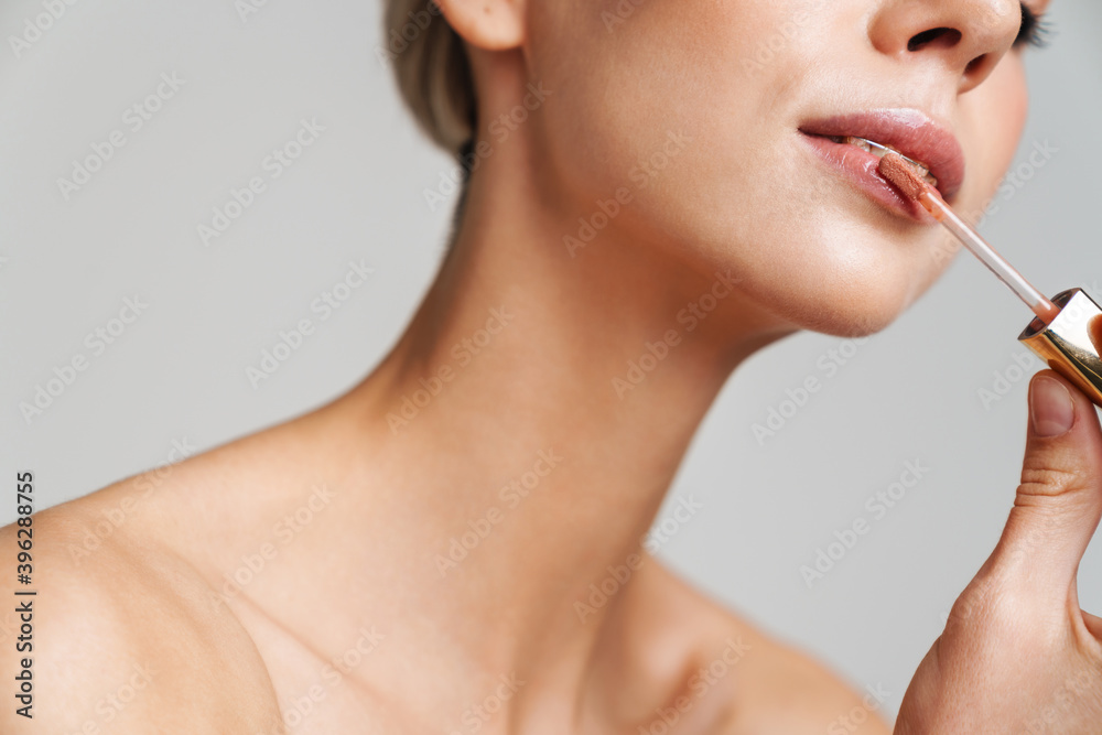 Sensual shirtless blonde girl applying lip gloss while doing makeup