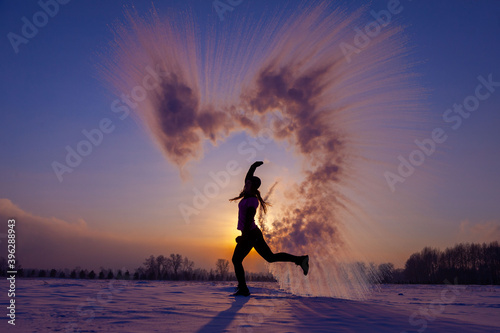 Silhouette of a sports girl at sunset in winter. Woman splashed boiling water on cold air.