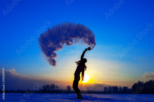 Silhouette of a sports girl at sunset in winter. Woman splashed boiling water on cold air.
