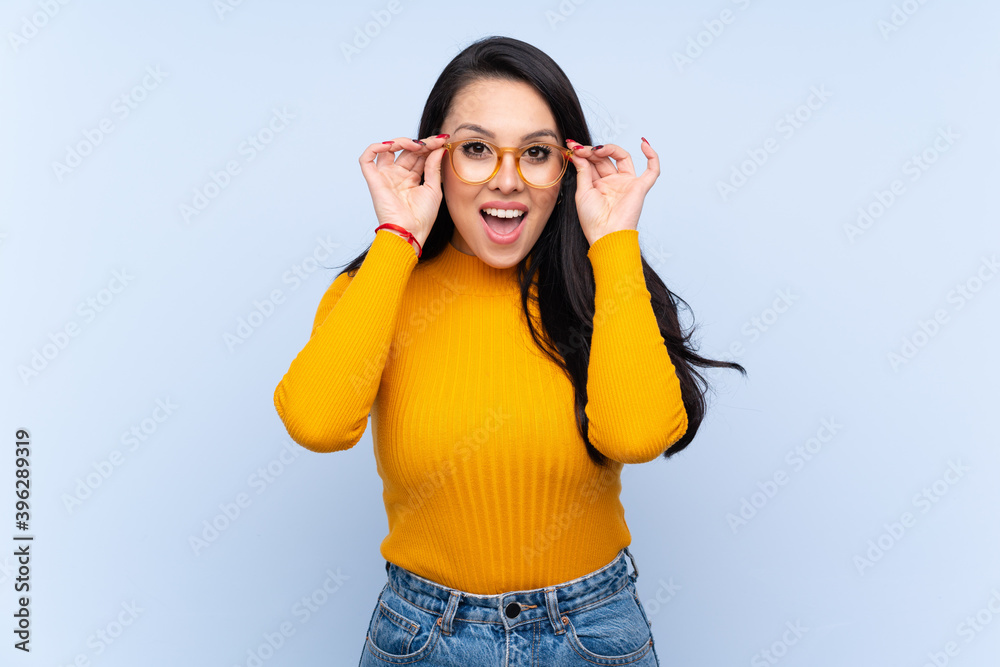 Young Colombian girl over isolated blue background with glasses and surprised Young Colombian girl over isolated blue background with glasses and surprised