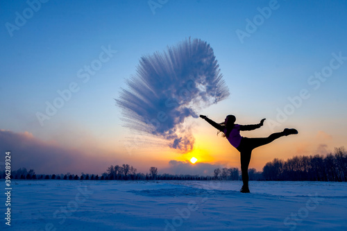 Silhouette of a sports girl at sunset in winter. Woman splashed boiling water on cold air.