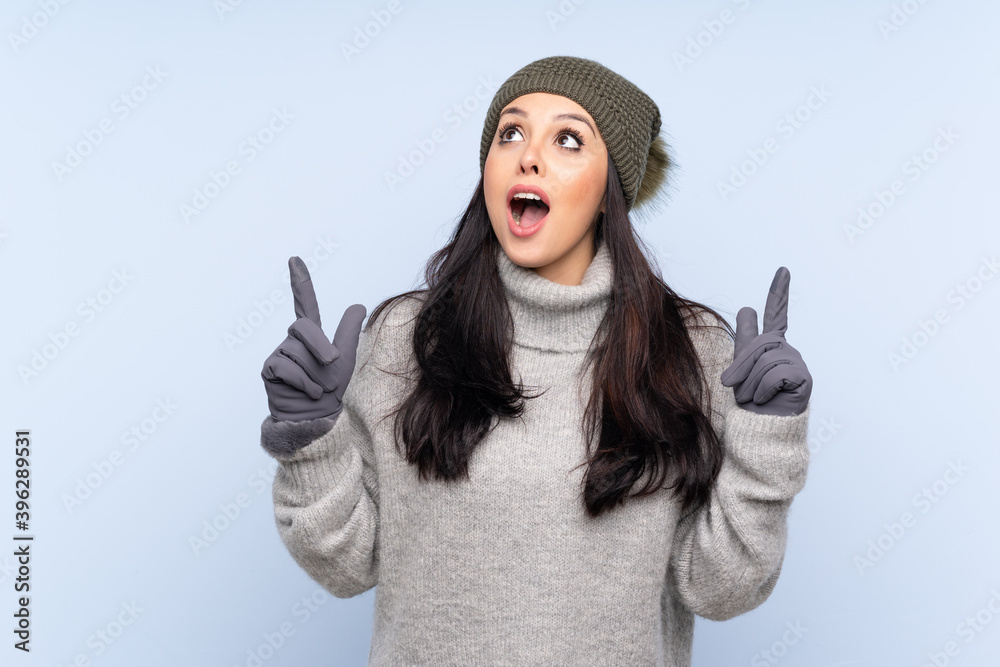 Young Colombian girl with winter hat over isolated blue background pointing with the index finger a great idea Young Colombian girl with winter hat over isolated blue background pointing with the index finger a great idea