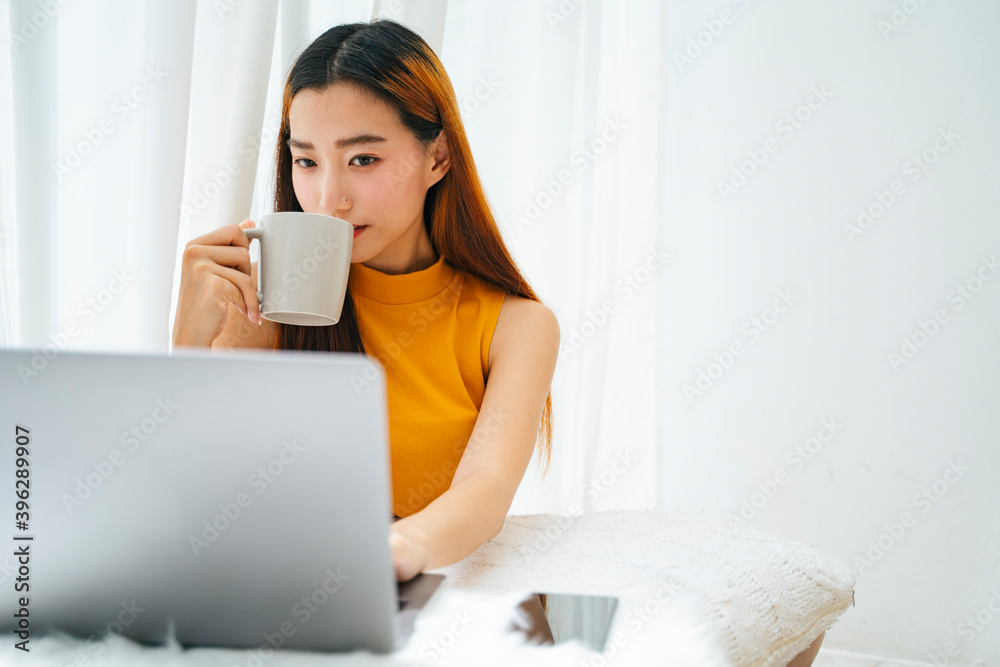 Asian woman drinking cup of water and using laptop computer at home. Asian woman drinking cup of water and using laptop computer at home.