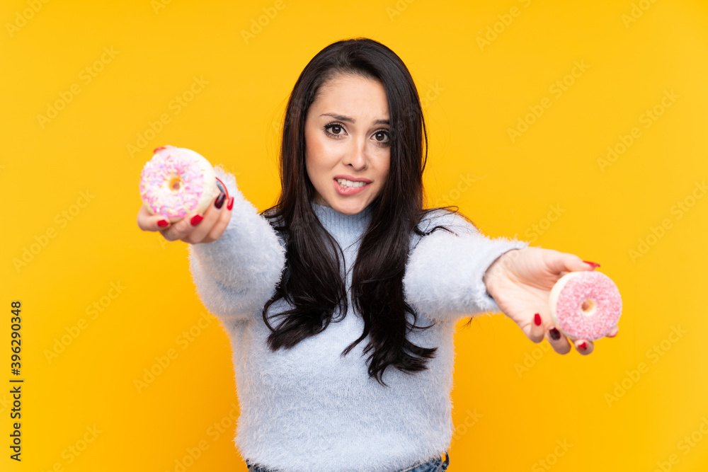 Young Colombian girl over isolated yellow background holding a donut and sad Young Colombian girl over isolated yellow background holding a donut and sad