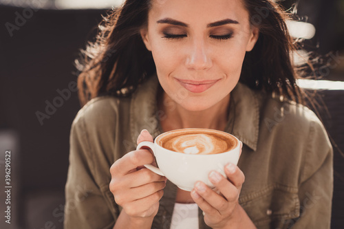Photo portrait of woman inhaling aroma of coffee holding cup in two hands in restaurant outside