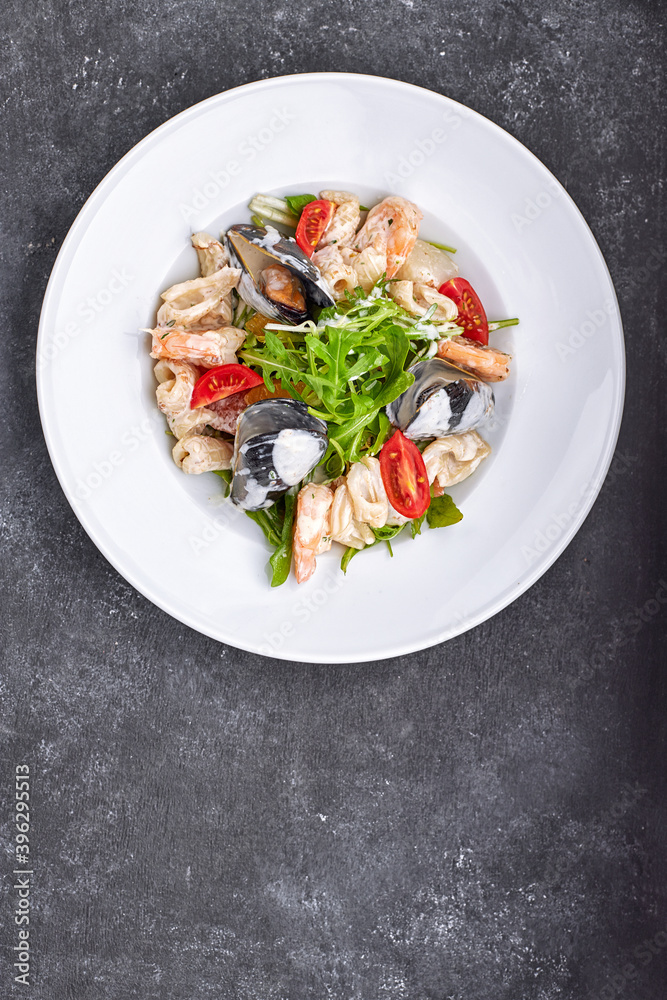 Seafood salad with mussels, squid, shrimp, on a round white plate, on a gray background