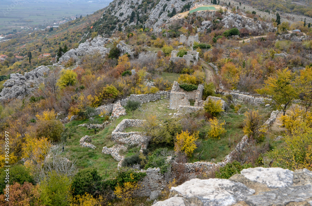 Ruins of medieval city in nature. Walls of old town on the hill in autumn. Fortress in forest.