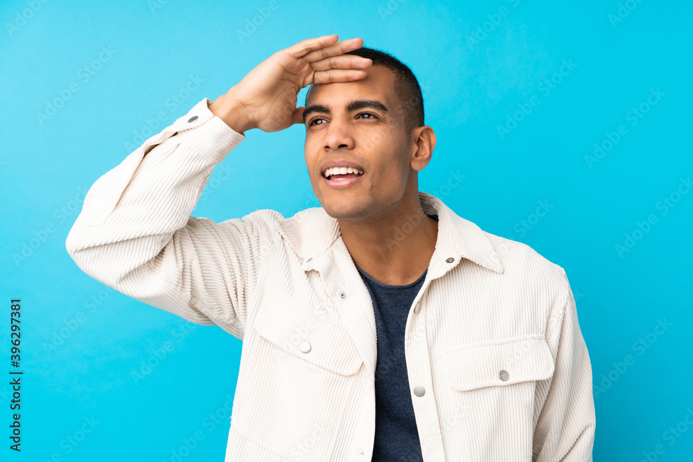 Young African American man over isolated blue background looking far away with hand to look something Young African American man over isolated blue background looking far away with hand to look something