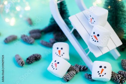 marshmallow snowmen ride on a sled on a turquoise background in Christmas decorations