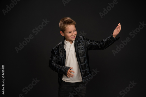 Obraz na plátně Pretty 10 year old boy in acting wearing suit school looks sideways with one arm theatrical up isolated on black background