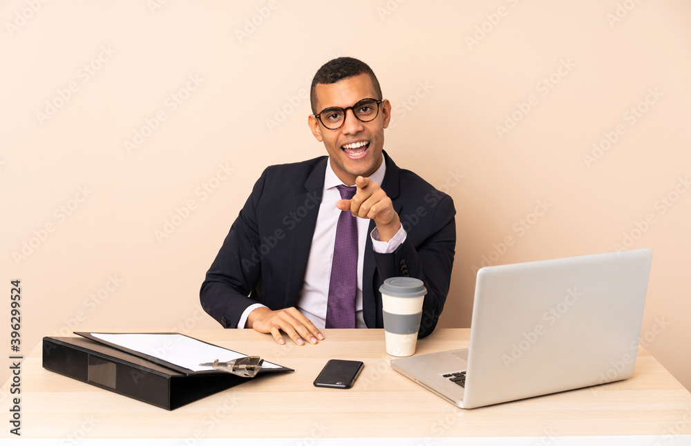 Young business man in his office with a laptop and other documents surprised and pointing front Young business man in his office with a laptop and other documents surprised and pointing front
