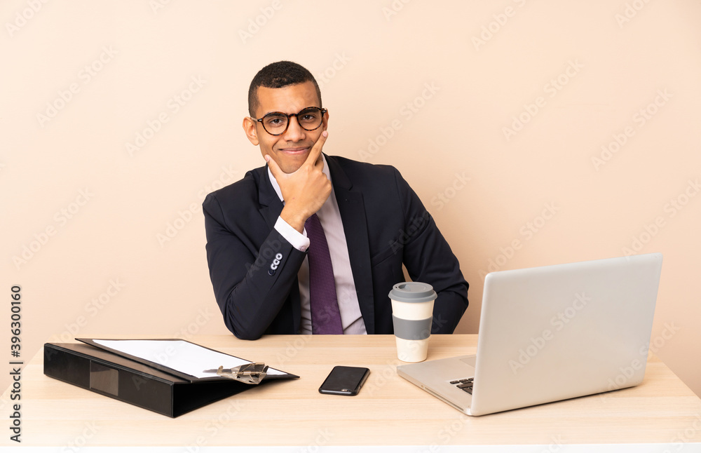 Young business man in his office with a laptop and other documents smiling Young business man in his office with a laptop and other documents smiling