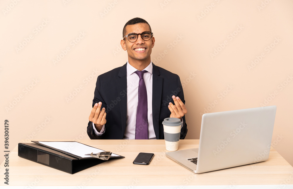 Young business man in his office with a laptop and other documents making money gesture Young business man in his office with a laptop and other documents making money gesture