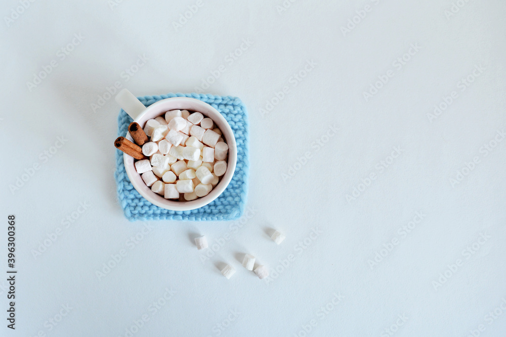Light blue handmade knitted coaster, cup with marshmallows and cinnamon over white Light blue handmade knitted coaster, cup with marshmallows and cinnamon over white