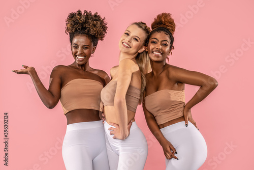 Group of smiling young women standing together on pink pastel studio background.