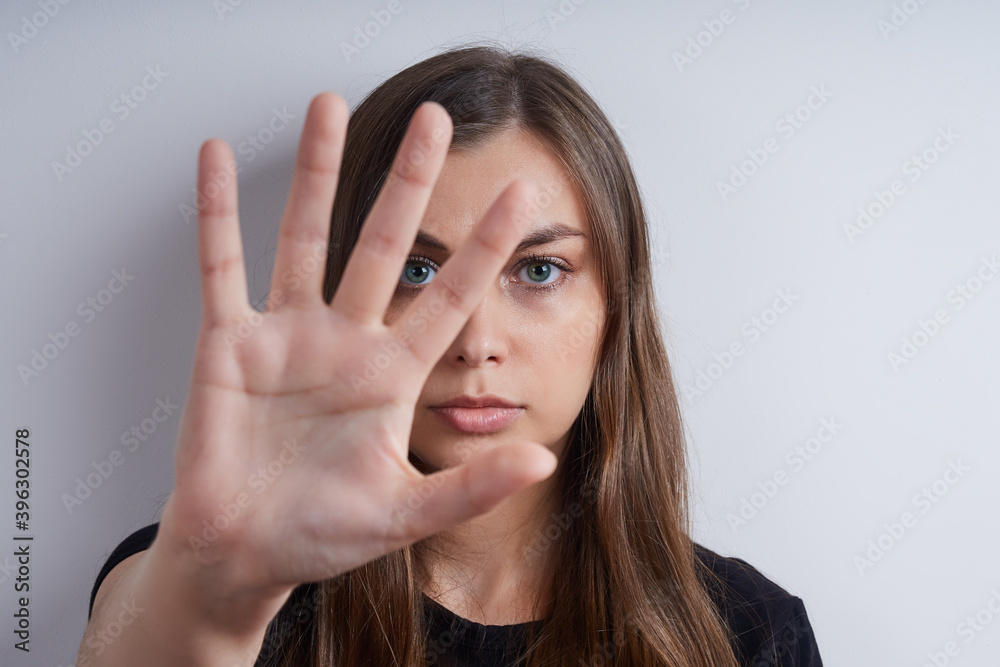 Portrait of a young serious woman in a black shirt, on a gray background, showing a stop symbol with her hand Portrait of a young serious woman in a black shirt, on a gray background, showing a stop symbol with her hand