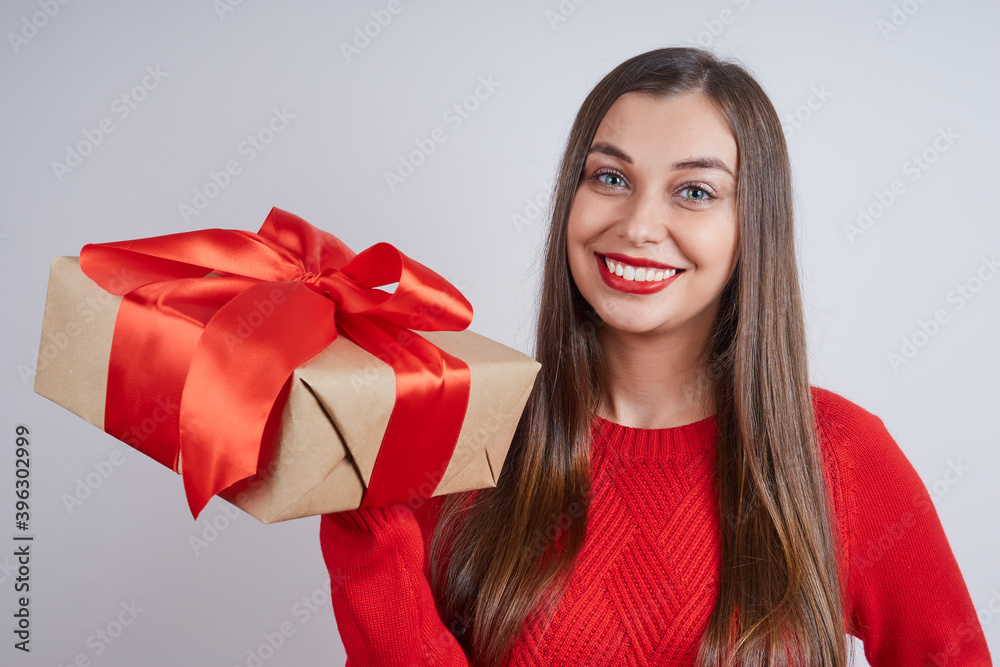 Joyful young woman in a red sweater holding a gift box, against gray background. Holiday concept, Christmas, New Year Joyful young woman in a red sweater holding a gift box, against gray background. Holiday concept, Christmas, New Year