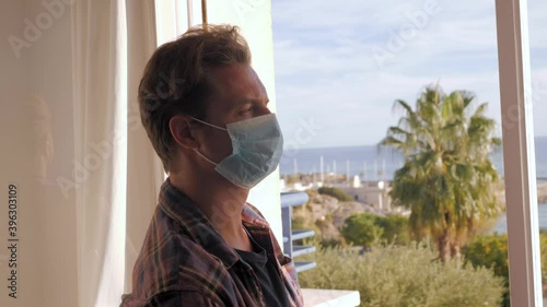 Middle aged man on the balcony of the house during the covid-19 outbreak lockdown. male with medical mask, worried and tired face looking at the street depressed in quarantine. Isolation concept