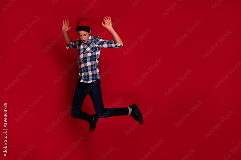 Young expressive teenager jumping over red background.