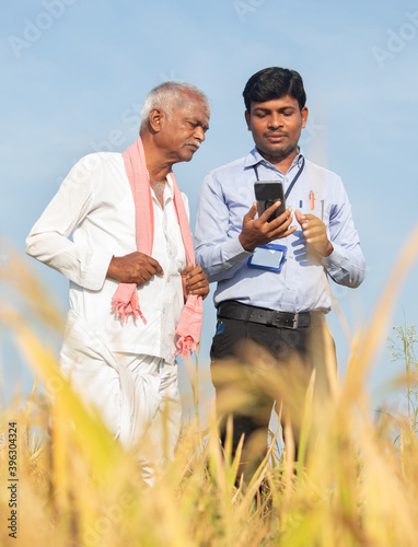 Konstfotografi Farmer and banker or corporate government officer discussing by looking into mobile phone about crop yield, credit and loan subsidy at agriculture farmland during hot sunny day