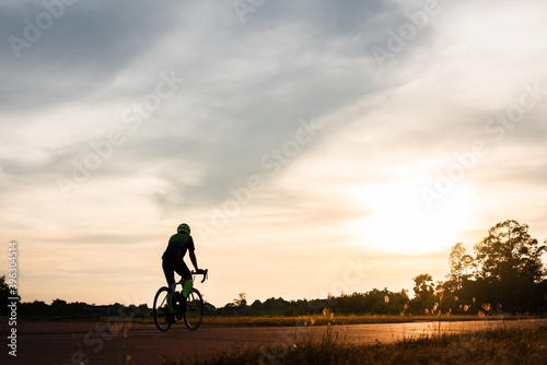 Backside of cyclist ride bicycle on sunset time in public park. Sport and active life concept.