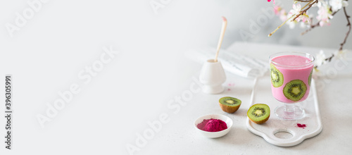 Pink matcha smoothie banner. Matcha smoothie with banana and kiwi in a glass on light background with sakura branches. Copy space.