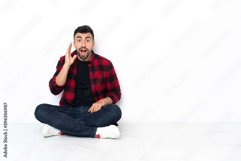 Young handsome man sitting on the floor with surprise and shocked facial expression Young handsome man sitting on the floor with surprise and shocked facial expression