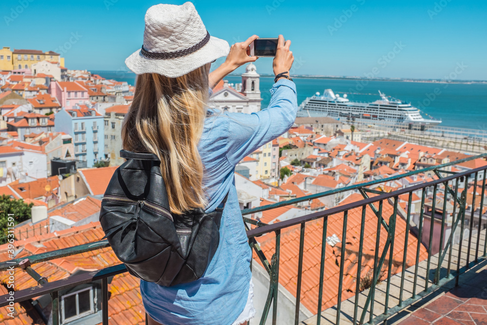 Young traveler woman with smartphone takes pictures in Lisbon of city under sky summer