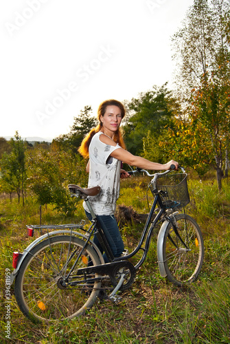 Woman with a bicycle in summer. Cycling in nature on an old vintage bicycle. Flowers, greens and forest in the background.