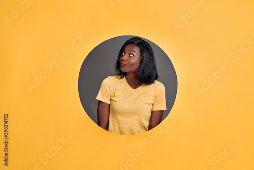 Beautiful young  woman in a round hole circle in orange background thinking about question, looking up, pensive expression. Smiling with thoughtful face. Copy space. © HBS