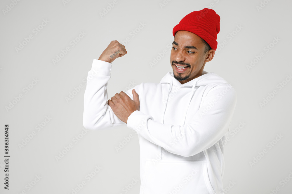 Strong puzzled young african american man 20s years old wearing basic casual streetwear hoodie standing showing biceps muscles looking camera isolated on white colour wall background studio portrait. Strong puzzled young african american man 20s years old wearing basic casual streetwear hoodie standing showing biceps muscles looking camera isolated on white colour wall background studio portrait.