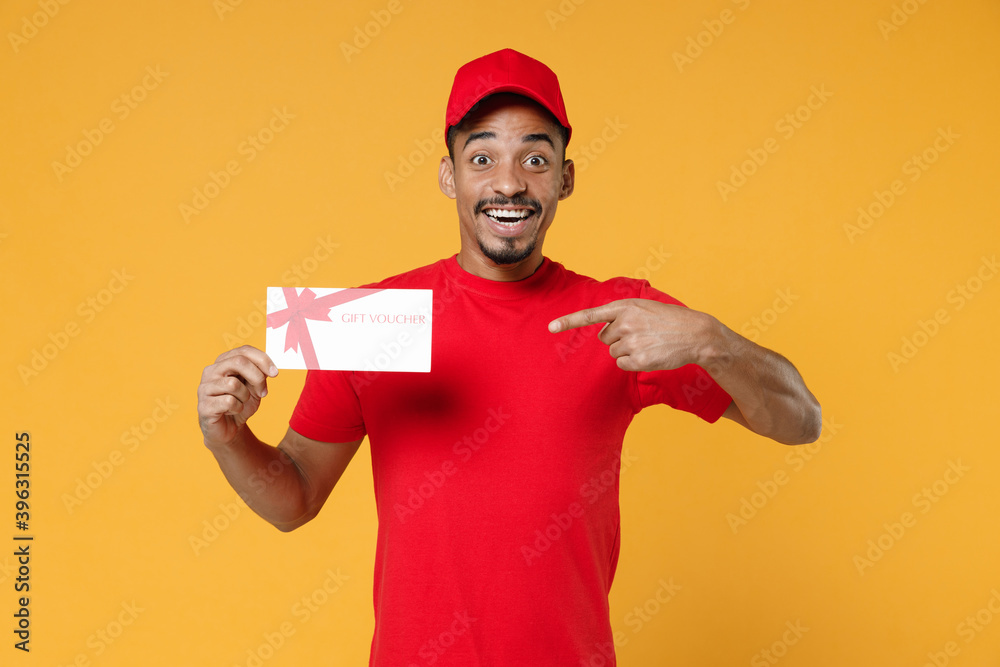 Delivery employee african man 20s in red cap blank print t-shirt uniform workwear work courier dealer service concept hold mockup gift certificate voucher coupon isolated on yellow background studio. Delivery employee african man 20s in red cap blank print t-shirt uniform workwear work courier dealer service concept hold mockup gift certificate voucher coupon isolated on yellow background studio.
