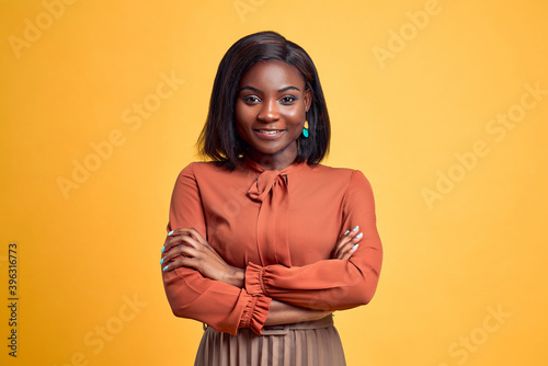 Advertising concept. Confident and smiling young african american woman crossed hands on chest, looking at camera and standing on yellow copy space background. photo