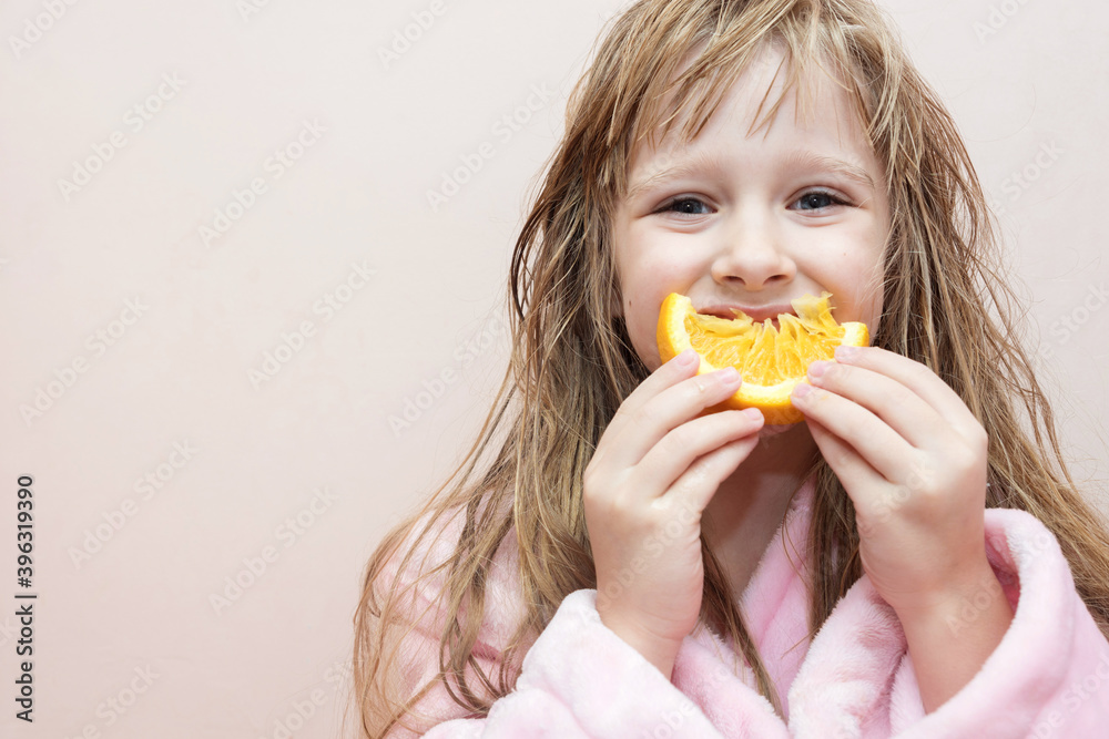 charming blonde girl with wet hair in a pink bath robe eating an orange