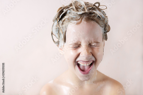 a little blonde girl in the bathroom with foam on her head laughs happily with her mouth open