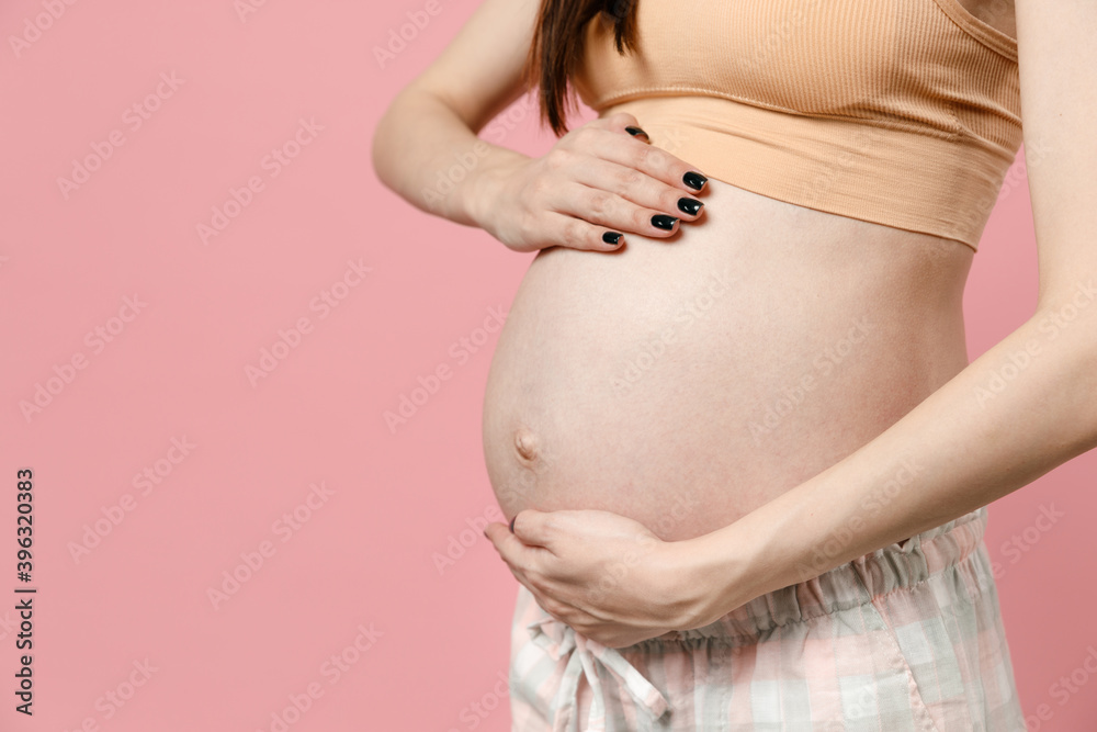 Close up cropped pregnant woman future mom in basic top stroking keeping hands on belly stomach tummy with baby isolated on pastel pink background studio Maternity family pregnancy gynecology concept Close up cropped pregnant woman future mom in basic top stroking keeping hands on belly stomach tummy with baby isolated on pastel pink background studio Maternity family pregnancy gynecology concept
