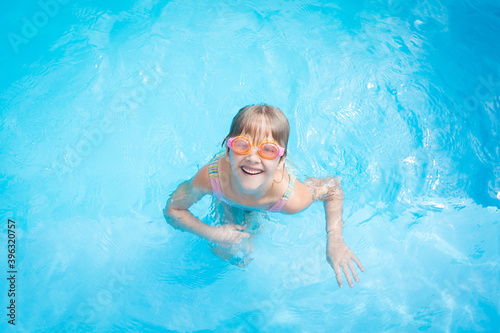 a little girl in a bathing suit and pink swimming glasses swims in a pool with blue water