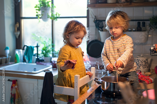 Small boy and girl indoors in kitchen at home, helping with cooking.