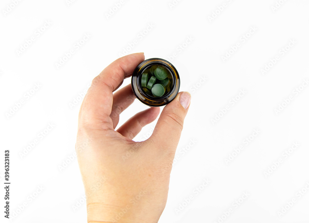Green spirulina tablets in a brown glass jar. Female hand holds pills vitamins. Green spirulina tablets in a brown glass jar. Female hand holds pills vitamins.