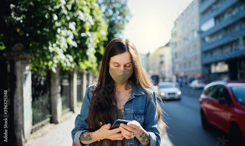 Mature woman with smartphone outdoors in city or town park, walking. Coronavirus concept.